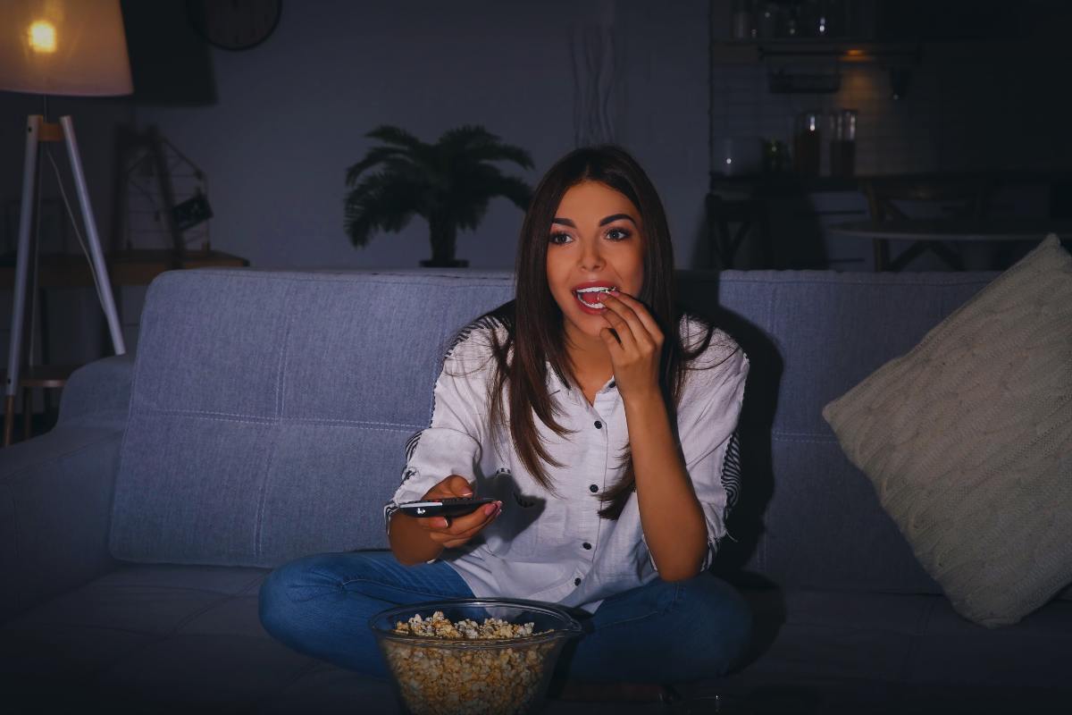 Ragazza che mangia popcorn su divano mentre guarda la televisione