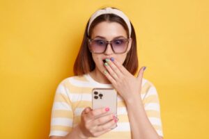 ragazza scioccata con una mano davanti alla bocca che guarda il cellulare